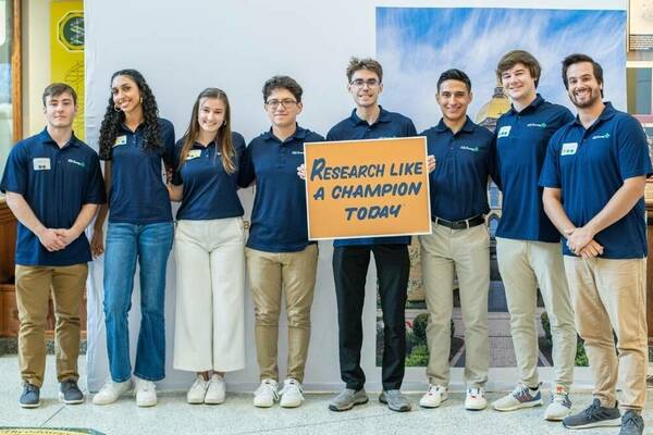 Levi Cherek ‘25 with group holding a "Research like a Champion Today" sign.