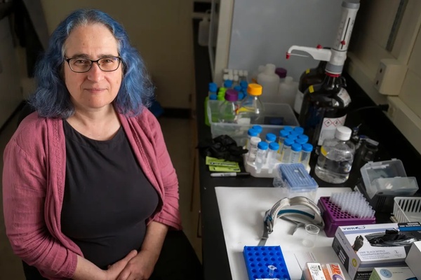 Marya Lieberman, wearing a black top with a pink sweater, smiles next to a set of samples.